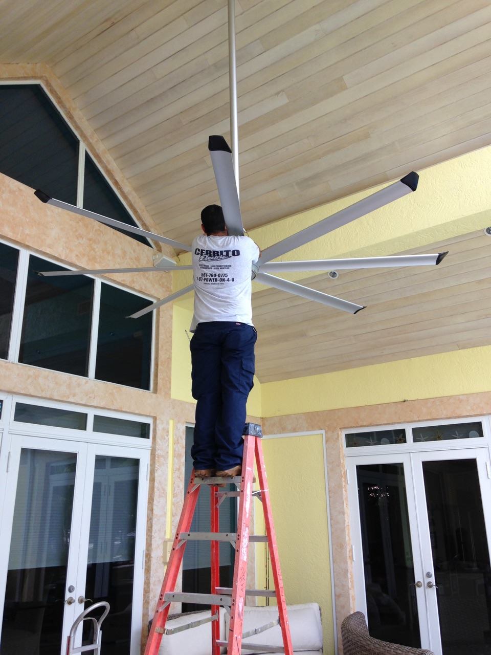 Cerrito Electric technician in a branded shirt installing a large ceiling fan in a home's covered patio